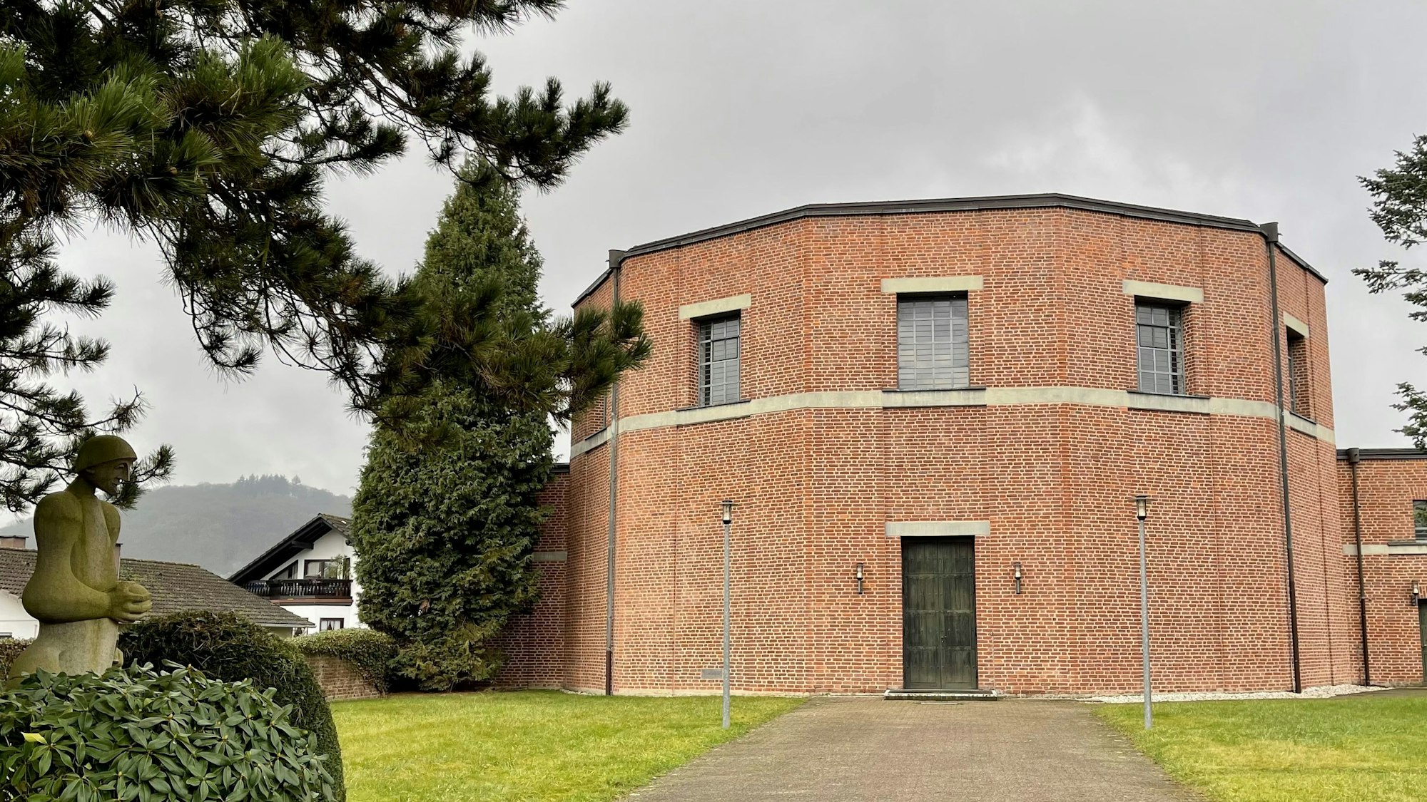 Ein runder Bau aus rotem Backstein auf einem parkähnlichen Grundstück.