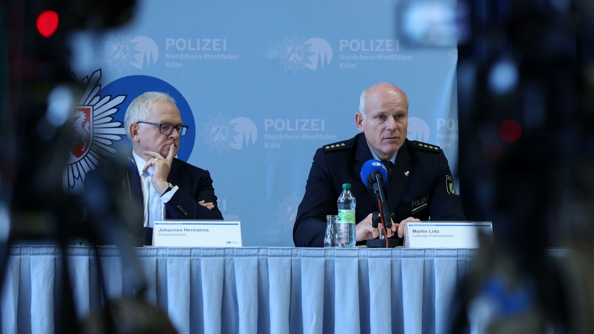 Johannes Hermanns und Martin Lotz sitzen auf einem Podium bei einer Pressekonferenz.