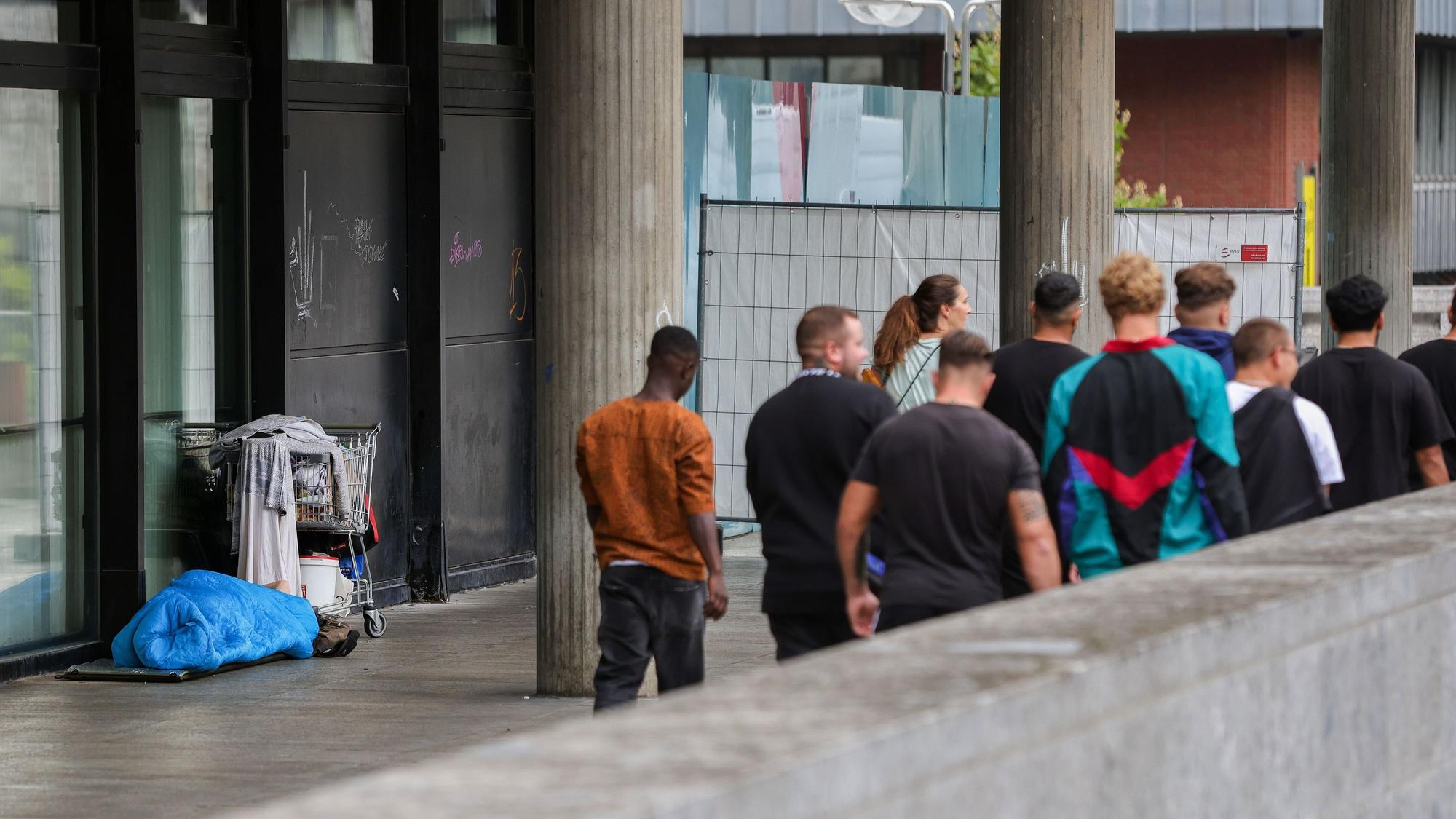 Ein wohl obdachloser Mensch liegt in der Nähe des Kölner Doms, daneben eine Gruppe junger Männer.
