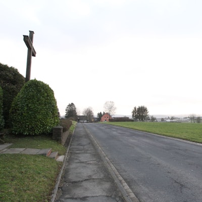 Ein Weg. Rechts ein Feld. Am Ende des Weges ein Haus. Ein paar Bäume auf dem Feld.