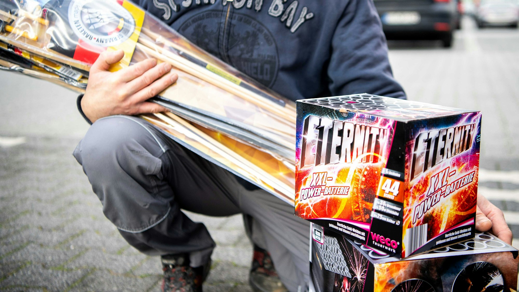 Die Detailaufnahme zeigt Feuerwerksartikel, die ein Mann auf einem Supermarktparkplatz präsentiert.