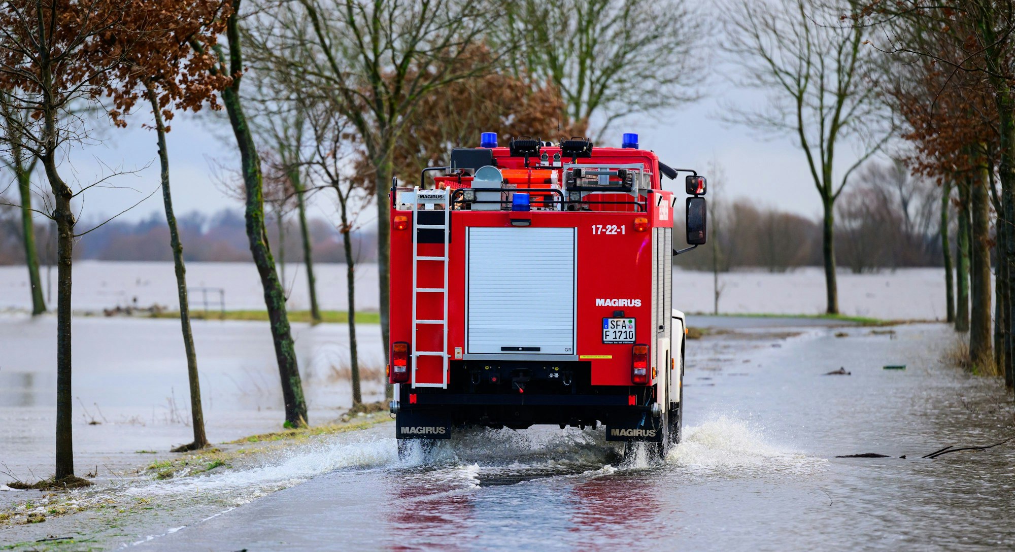 29.12.2023, Niedersachsen, Kirchwahlingen: Ein Fahrzeug der Feuerwehr fährt auf einer teilweise überfluteten Straße unweit der Aller. Die Hochwasserlage bleibt in vielen Regionen Niedersachsens angespannt. Foto: Philipp Schulze/dpa +++ dpa-Bildfunk +++