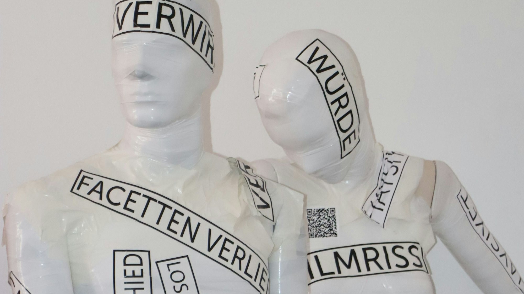 Zu sehen sind zwei weiße Schaufensterpuppen, die mit Worten beklebt sind.