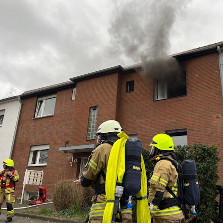 In einer Küche einer Wohngruppe für Jugendliche hat es gebrannt, Feuerwehrleute stehen als Rettungstrupp für ihre Kameraden vor dem Haus.