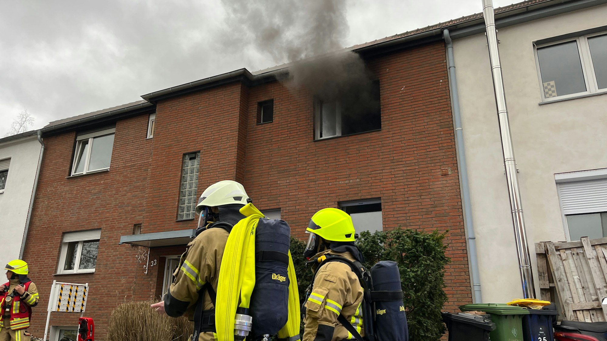 In einer Küche einer Wohngruppe für Jugendliche hat es gebrannt, Feuerwehrleute stehen als Rettungstrupp für ihre Kameraden vor dem Haus.