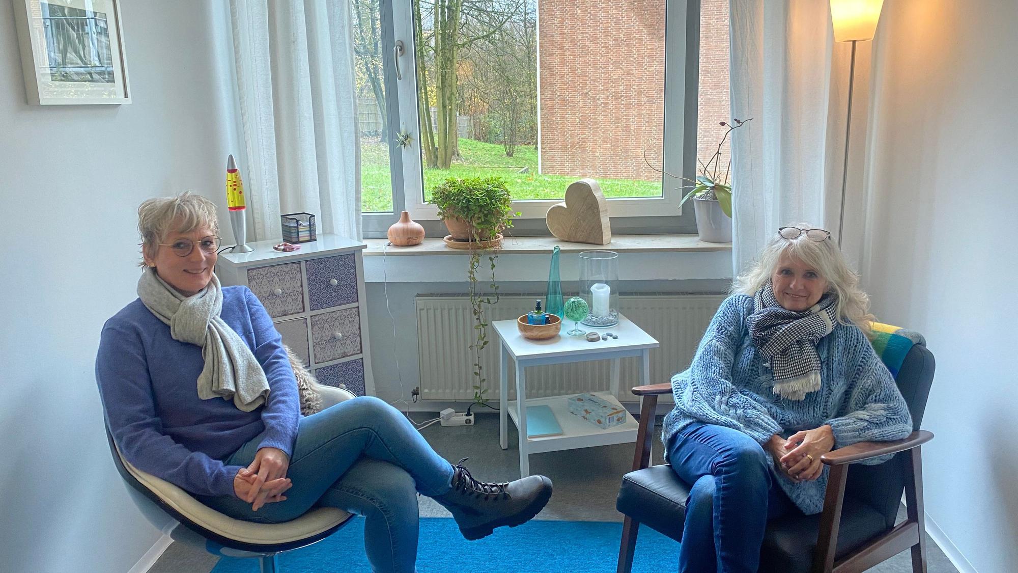 Zwei Frauen sitzen auf zwei Stühlen vor einem Fenster
