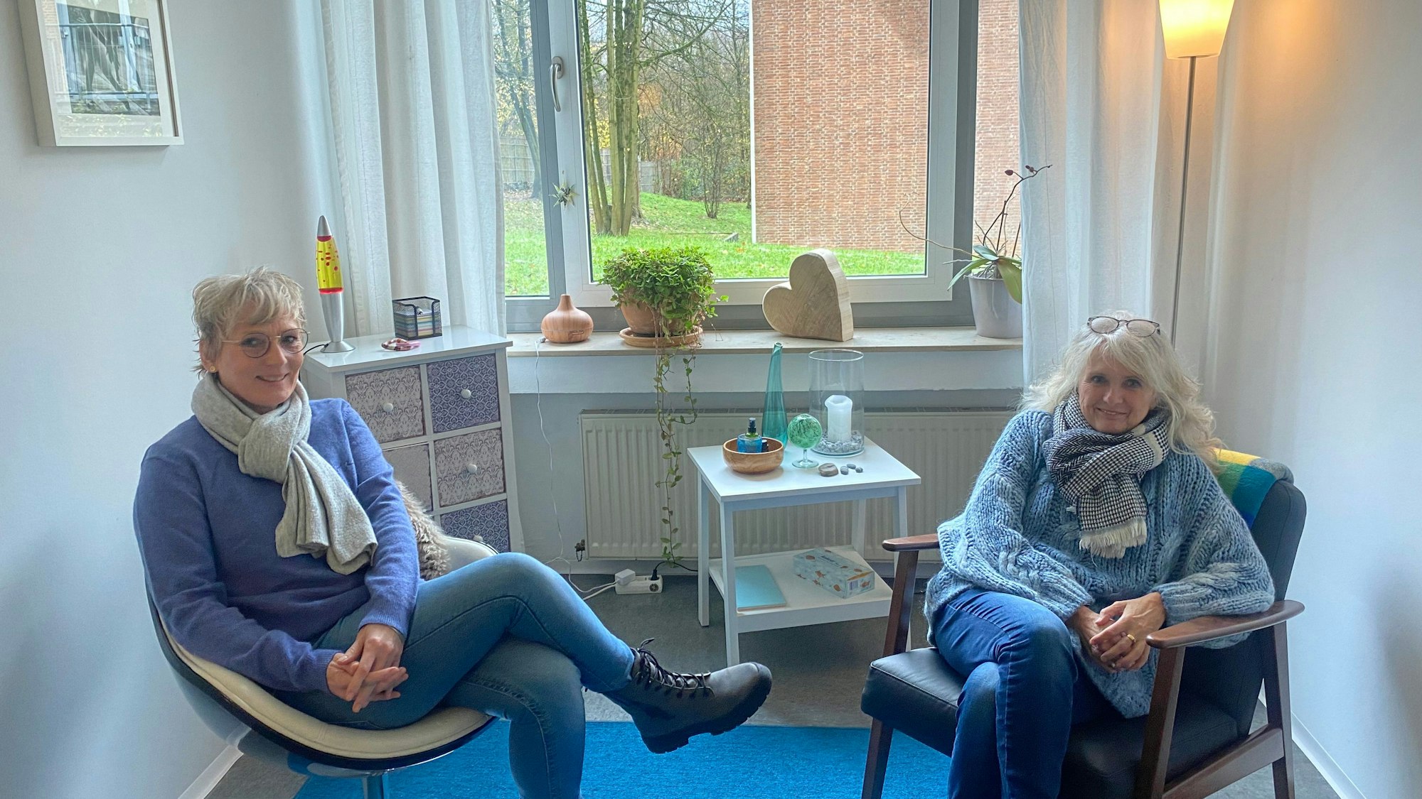 Zwei Frauen sitzen auf zwei Stühlen vor einem Fenster