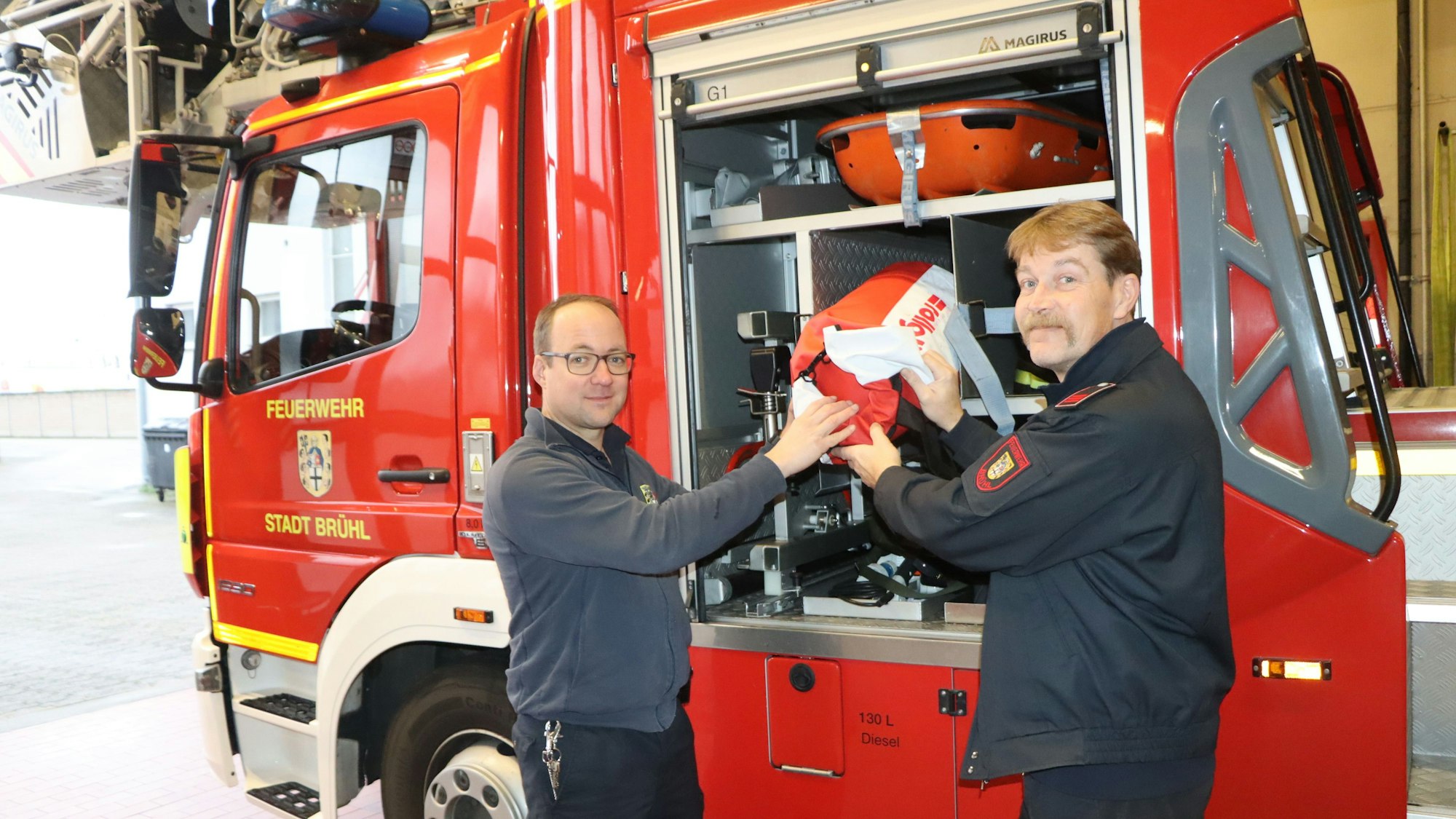 Zwei Feuerwehrleute prüfen Material vor einem Einsatzfahrzeug.