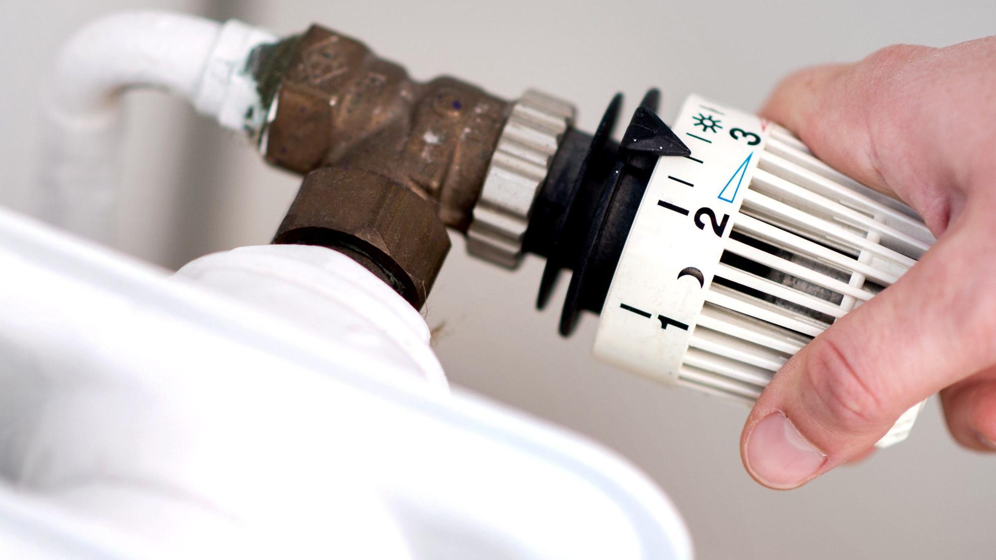 Eine Frau dreht am Thermostat eines Heizkörpers