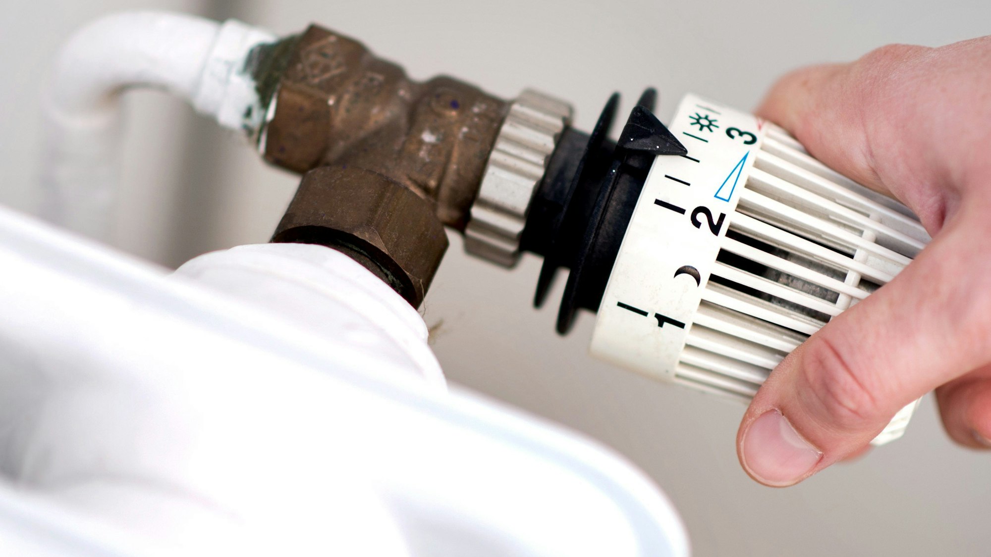 Eine Frau dreht am Thermostat eines Heizkörpers