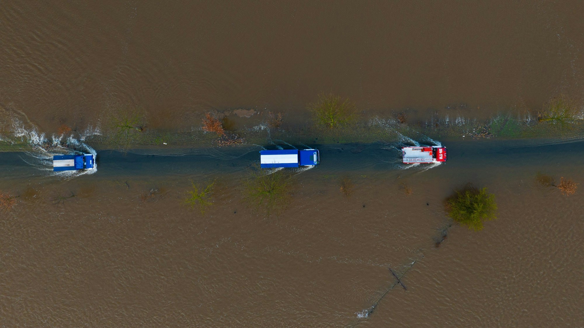 Ein Fahrzeug vom THW sowie der Feuerwehr fahren auf einer teilweise überfluteten Straße unweit der Aller (Aufnahme mit einer Drohne).
