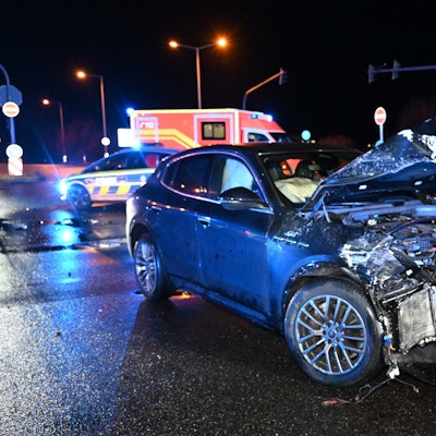Ein schwer beschädigter Maserati steht auf einer Straßenkreuzung. Im Hintergrund sind ein Polizeiwagen und ein Rettungswagen zu sehen