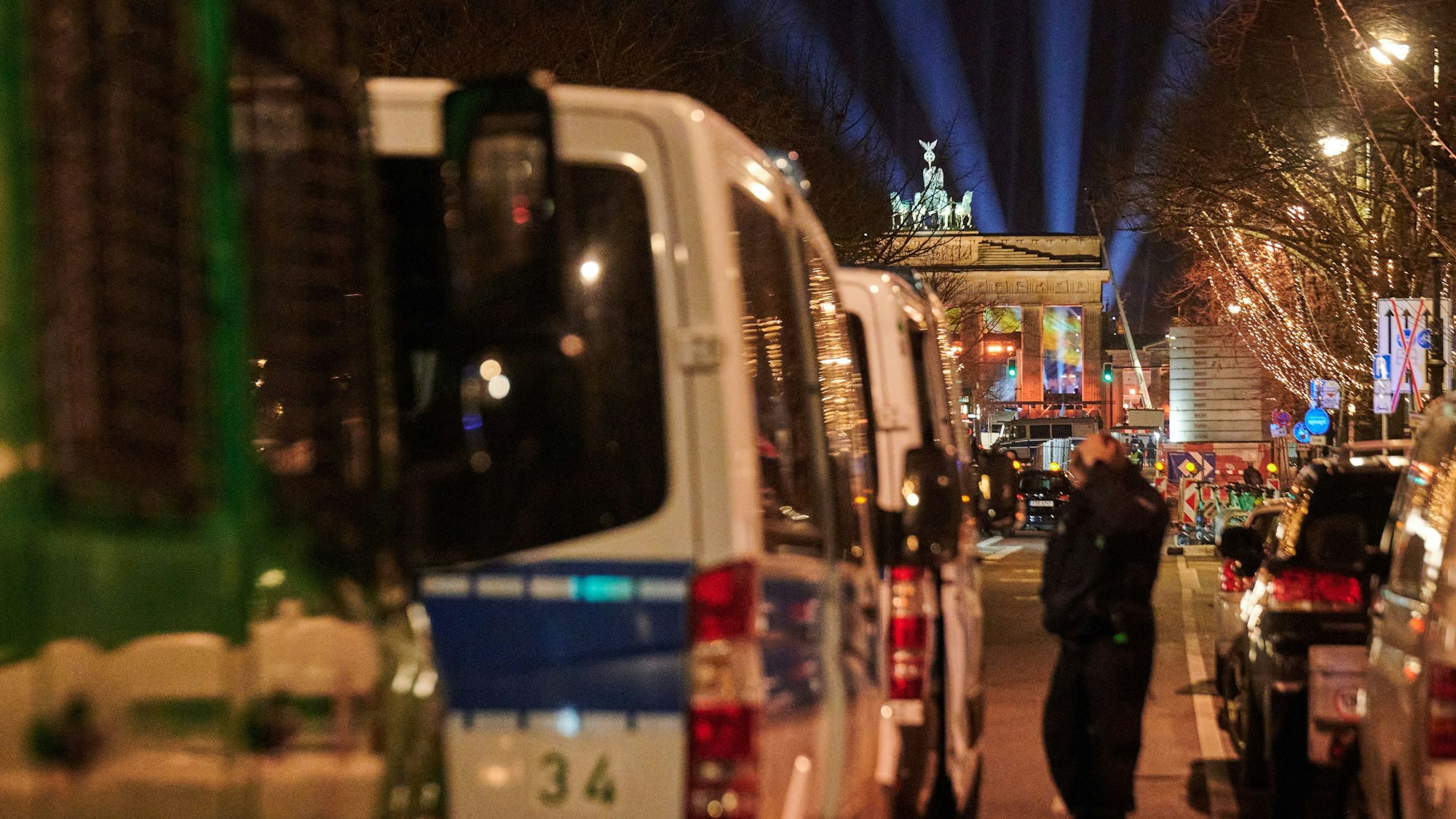 Polizeiwägen stehen unter den Linden, während Lichtstrahlen der Proben vor dem Brandenburger Tor darüber emporstrahlen. (Symbolbild)