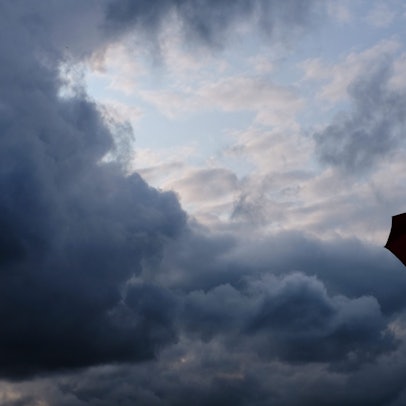 Ein Mann geht mit einem Regenschirm vor aufziehenden dunklen Wolken spazieren.
