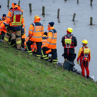 Mitglieder von Feuerwehr und DLRG stehen am Rand einer großen Wasserfläche.