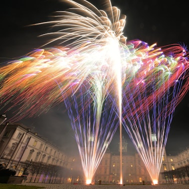 Die Lichter von bunte Feuerwerksraketen sind vor einer Häuserkulisse zu sehen.