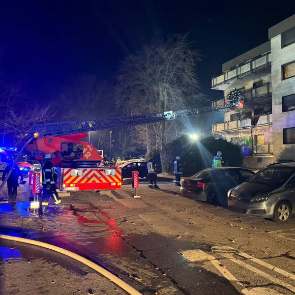 Über eine Drehleiter gelangen Feuerwehrleute auf einen Balkon eines mehrstöckigen Hauses.