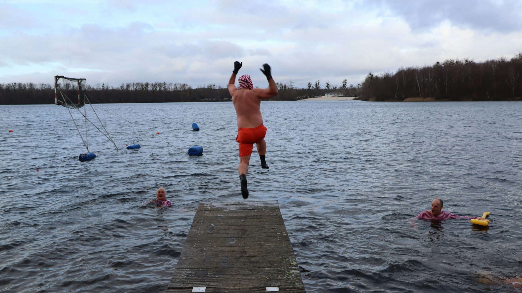 Ein Mann, bekleidet mit einer Badehose, spring von einem Steg in den Liblarer See.