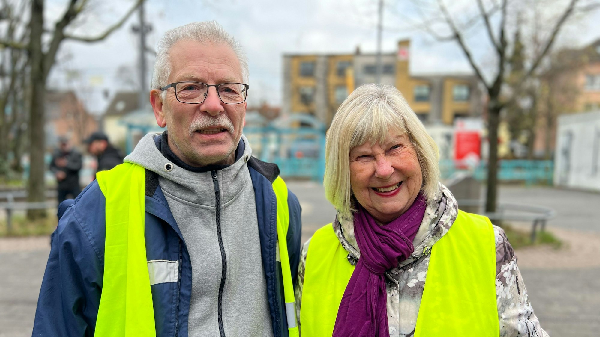 Ein Mann und eine Frau in gelben Warnwesten stehen in der Porzer Fußgängerzone.