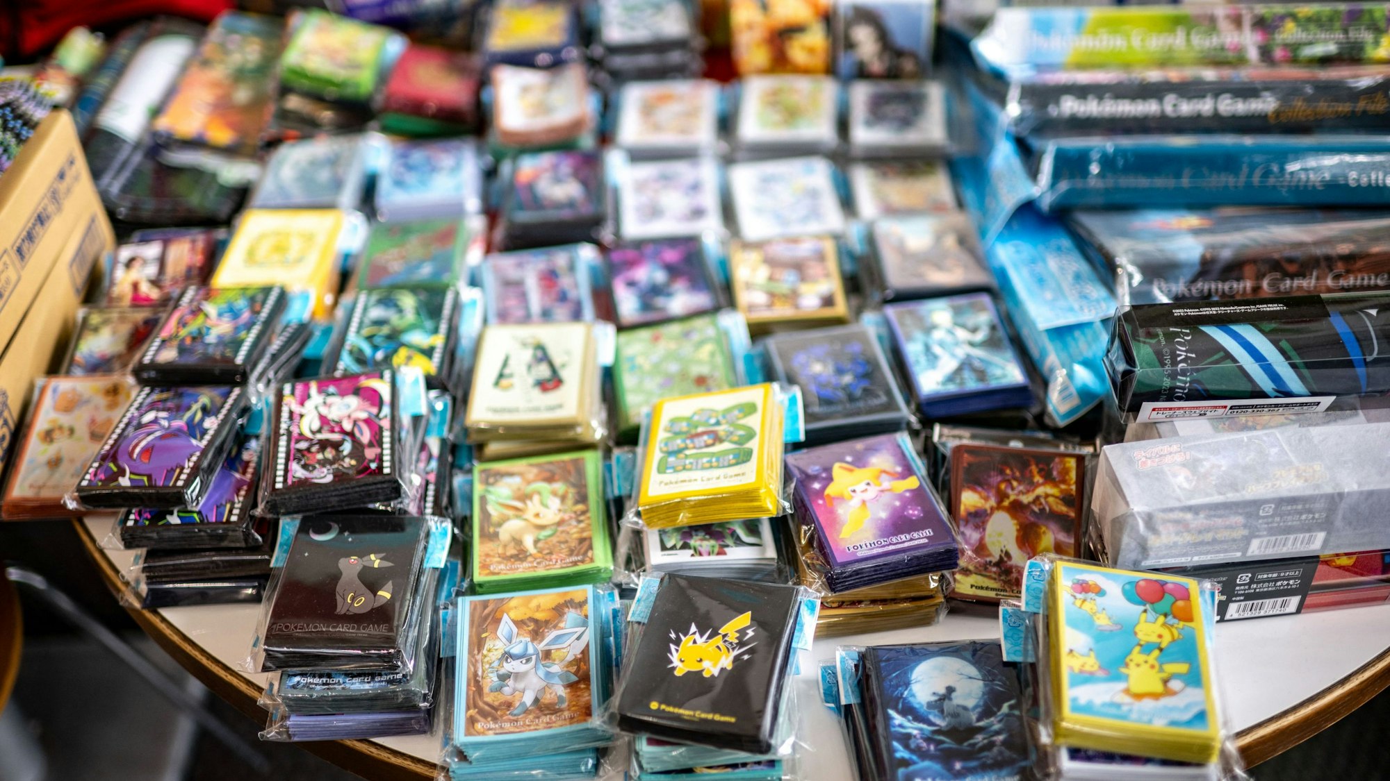 Auf einem Tisch sind eine Vielzahl an Pokémon-Karten inklusive Hüllen und weiterem Zubehört aufgetürmt.