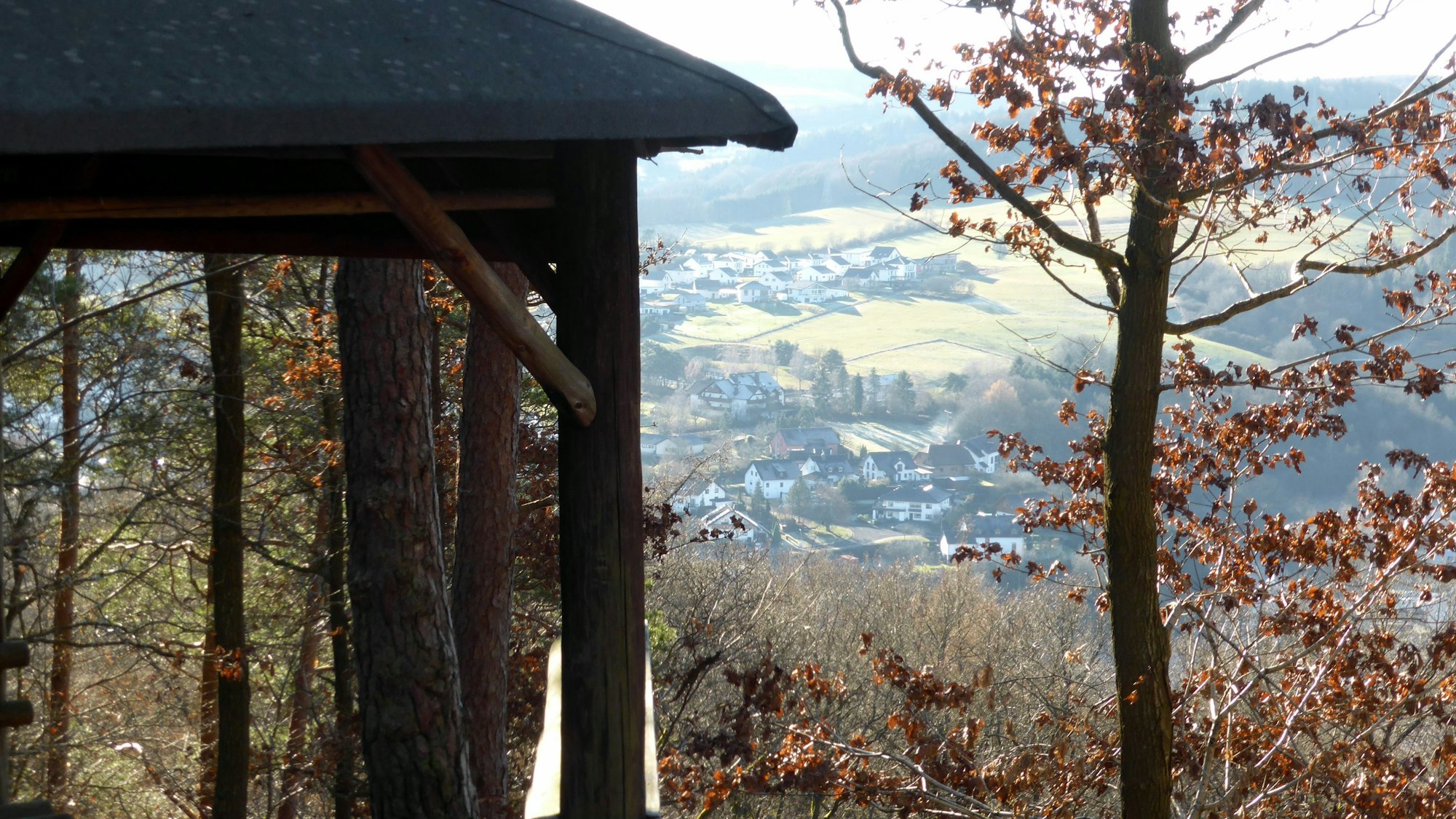 Im Vordergrund ist eine Waldhütte zu sehen. Im Hintergrund erstreckt sich ein mit Häusern gesprenkeltes Tal.