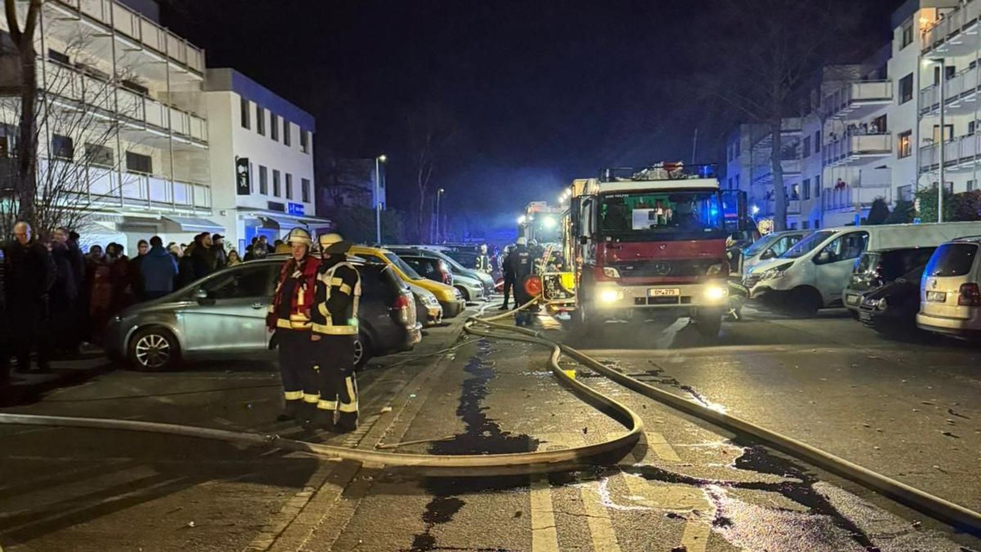 Auf dem Bild sind Feuerwehrleute und -autos in einem nächtlichen Einsatz zu sehen, im Hintergrund Blaulicht.