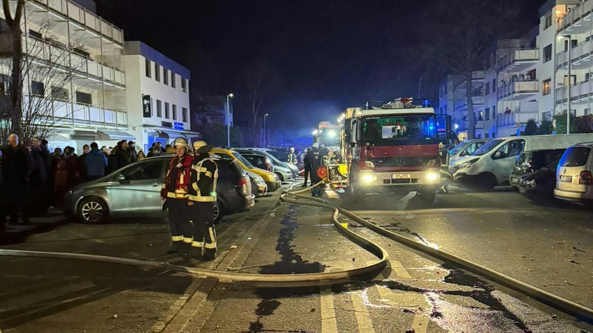 Auf dem Bild sind Feuerwehrleute und -autos in einem nächtlichen Einsatz zu sehen, im Hintergrund Blaulicht.