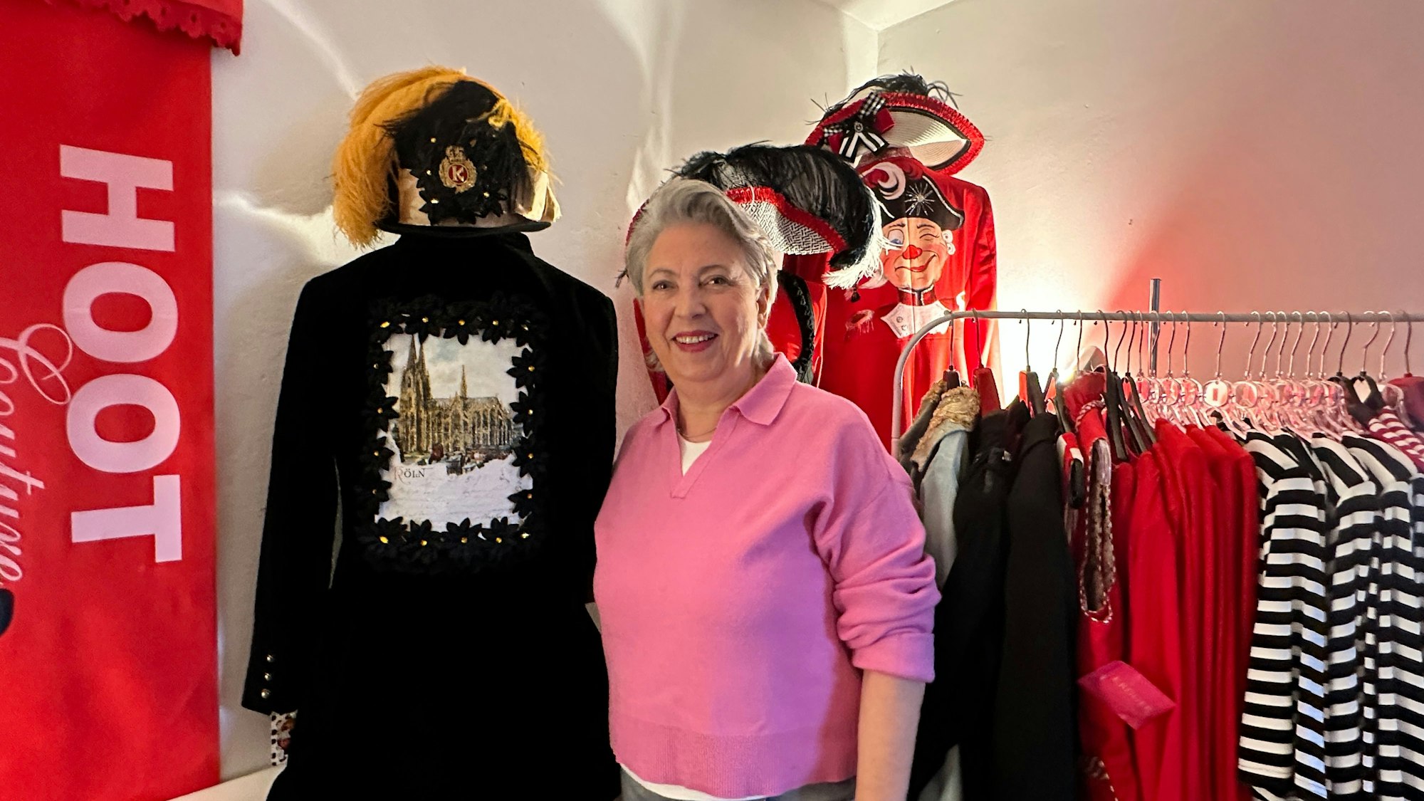 Eine Frau mit grauem kurzen Haar steht zwischen einer Schaufensterpuppe und einer Kleiderstange mit geringelten Oberteilen.