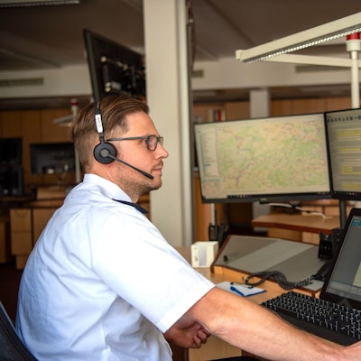 Nico Grocki, einer der Disponenten in der Rettungsleitstelle des Kreises Euskirchen, sitzt mit einem Headset auf dem Kopf an seinem Arbeitsplatz vor zahlreichen Monitoren.