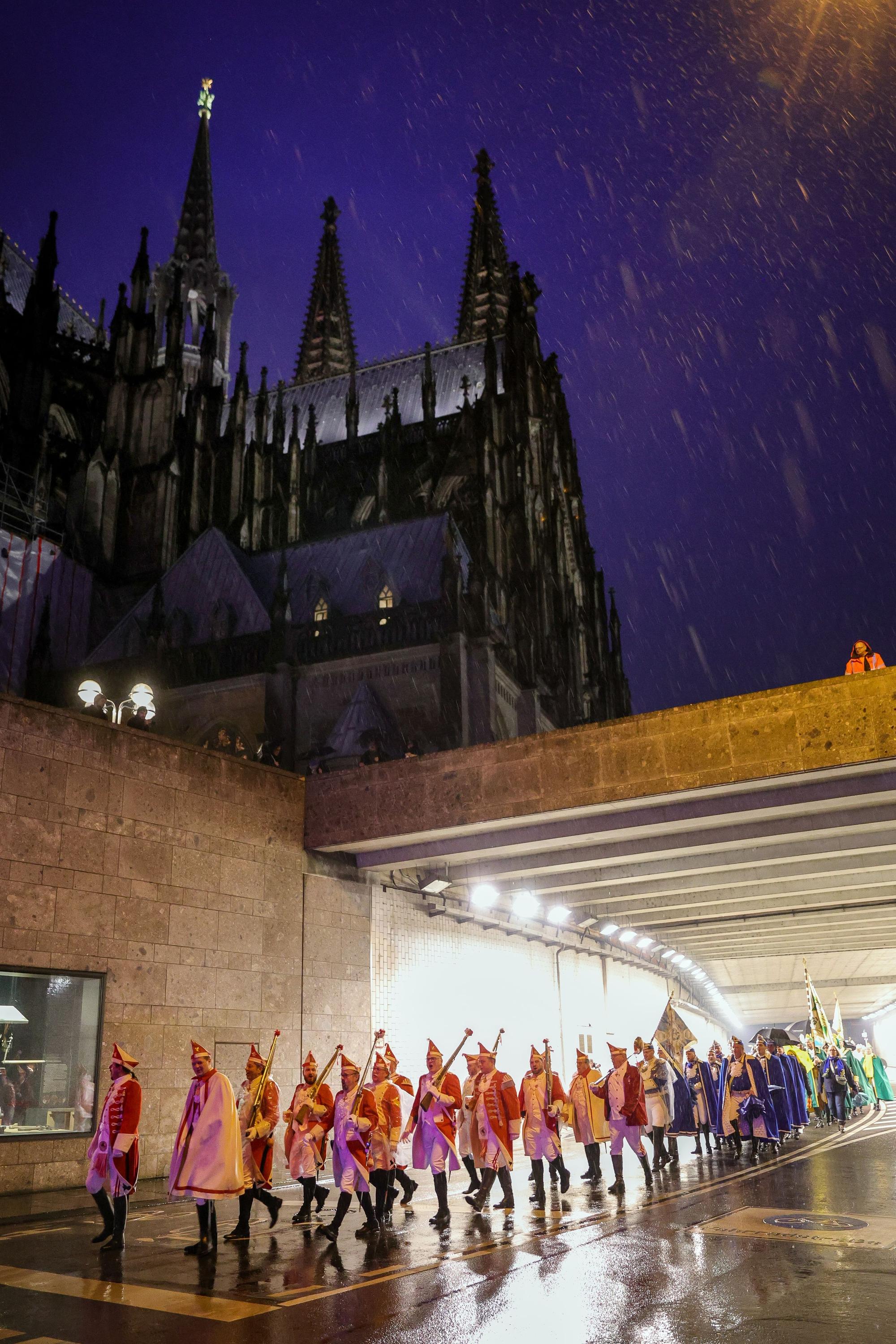 Menschen in Karnevalsuniformen gehen am Dom vorbei.