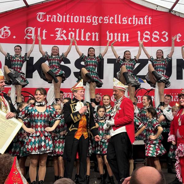 Die Volkssitzung 2023 der KG Alt-Köllen im Zelt auf dem Neumarkt: Präsident der KG spricht mit Festkomitee-Chef Christof Kuckelkorn, im Hintergrund hebt das Tanzkorps Mariechen in die Höhe.