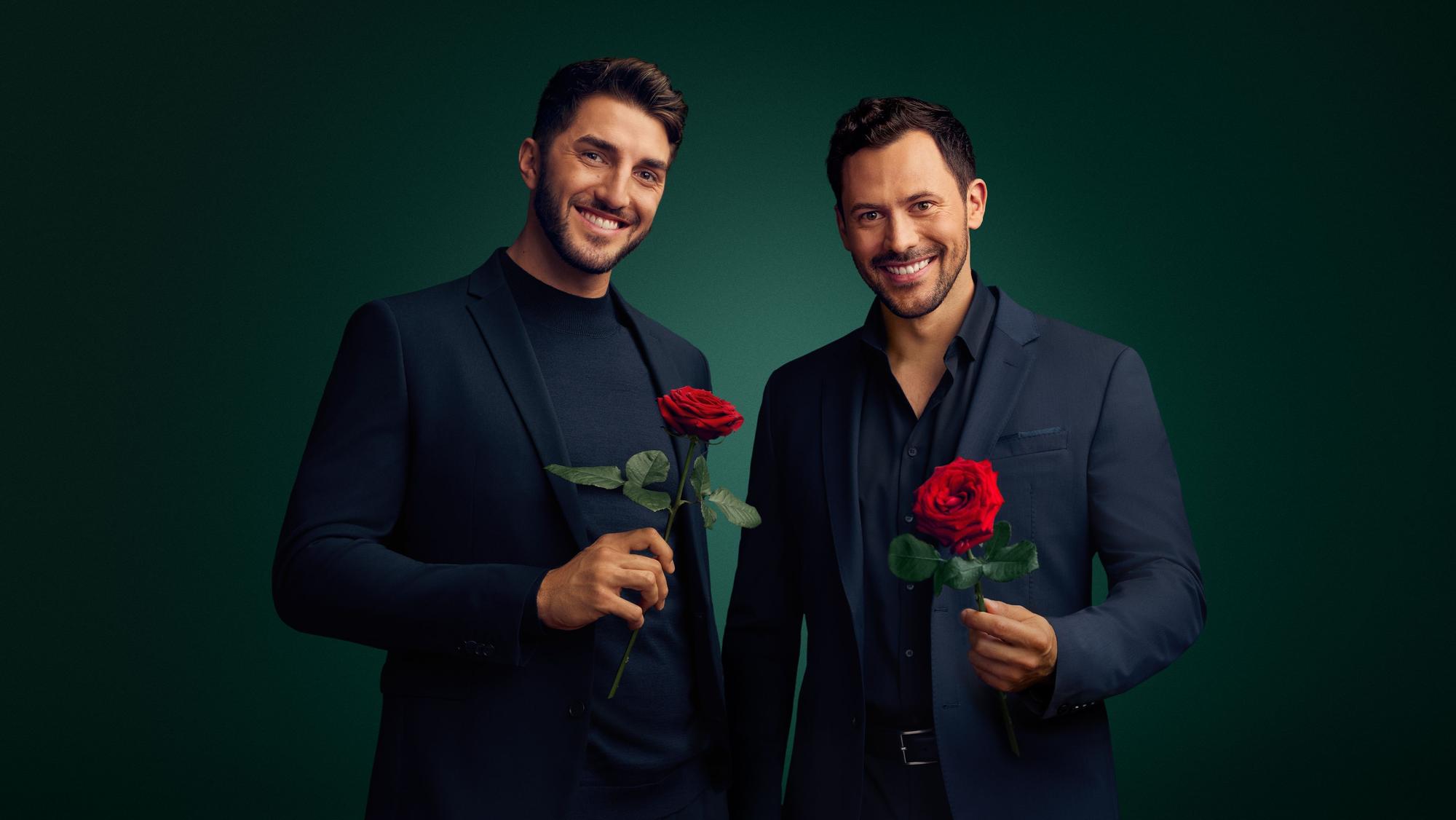 Zwei Männer mit blauen Sakkos halten jeweils eine rote Rose in der Hand.