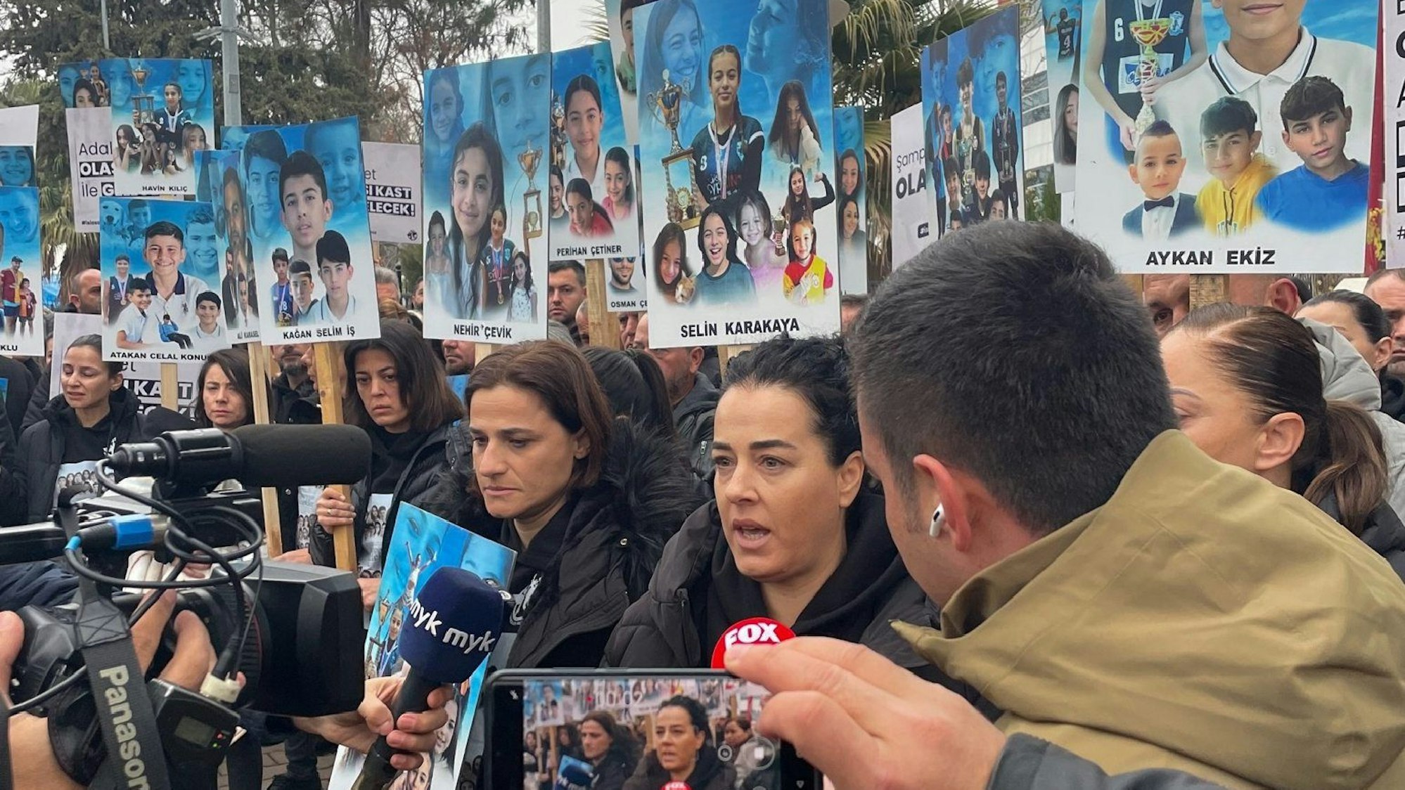 Angehörige stehen vor dem Gerichtsgebäude im südosttürkischen Adiyaman und halten Bilder ihrer Kinder hoch, dir bei dem Erdbeben im vergangenen Februar getötet wurden.