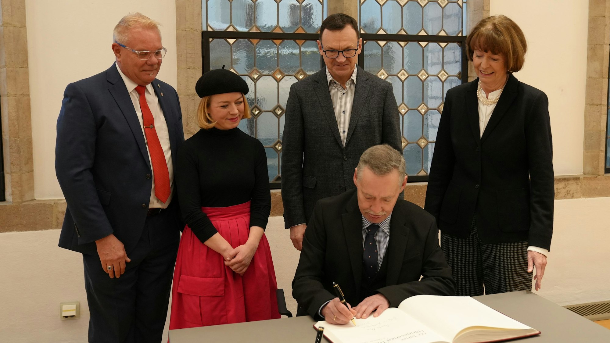 Ein Mann, der in ein Gästebuch schreibt, hinter ihm stehen zwei Männer und zwei Frauen