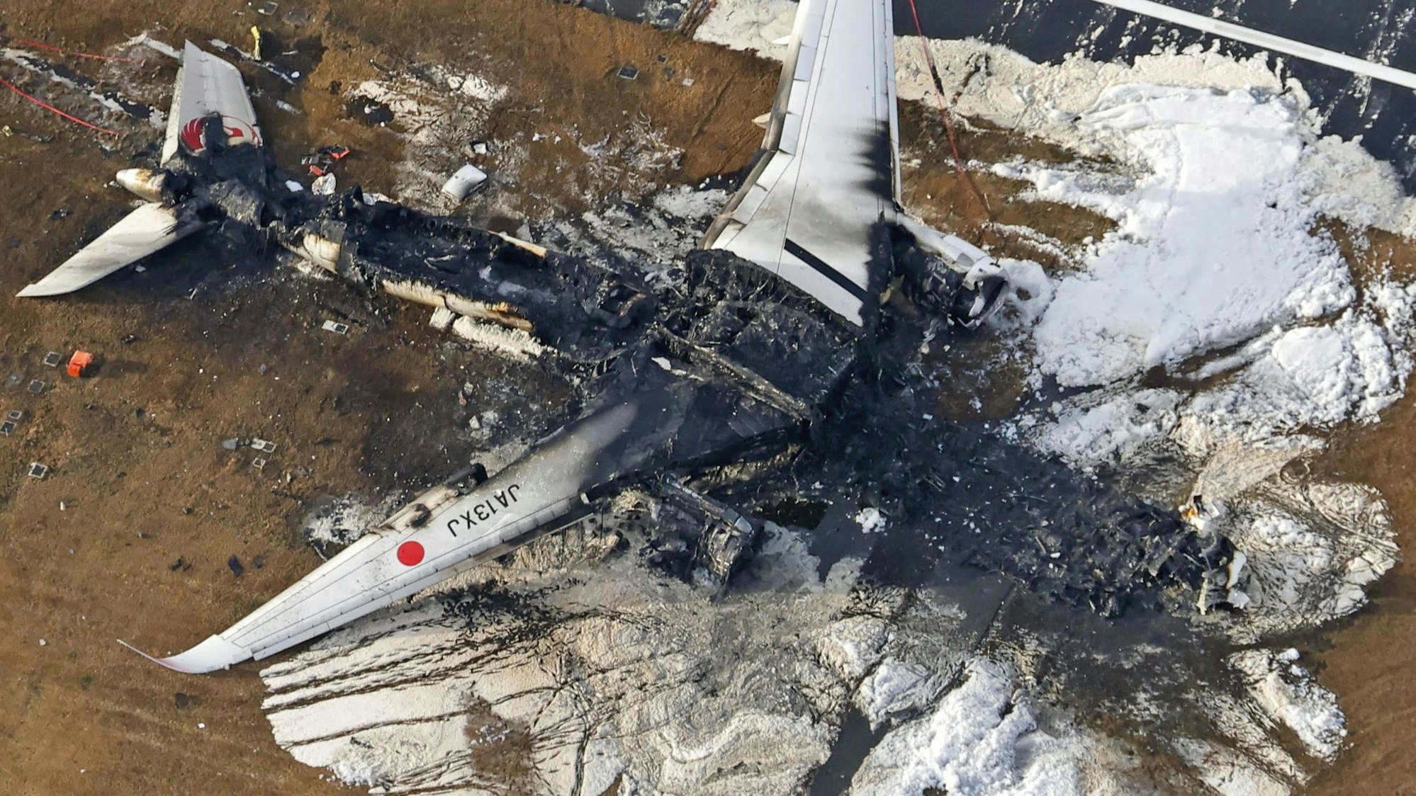 Die Luftaufnahme zeigt das ausgebrannte Flugzeug der Japan Airlines auf dem Flughafen Haneda. Behörden wollen nun die Schuldfrage klären.