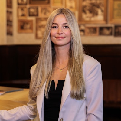 Eine Frau mit blonden langen Haaren steht vor einem Tisch mit einem Ventilator.