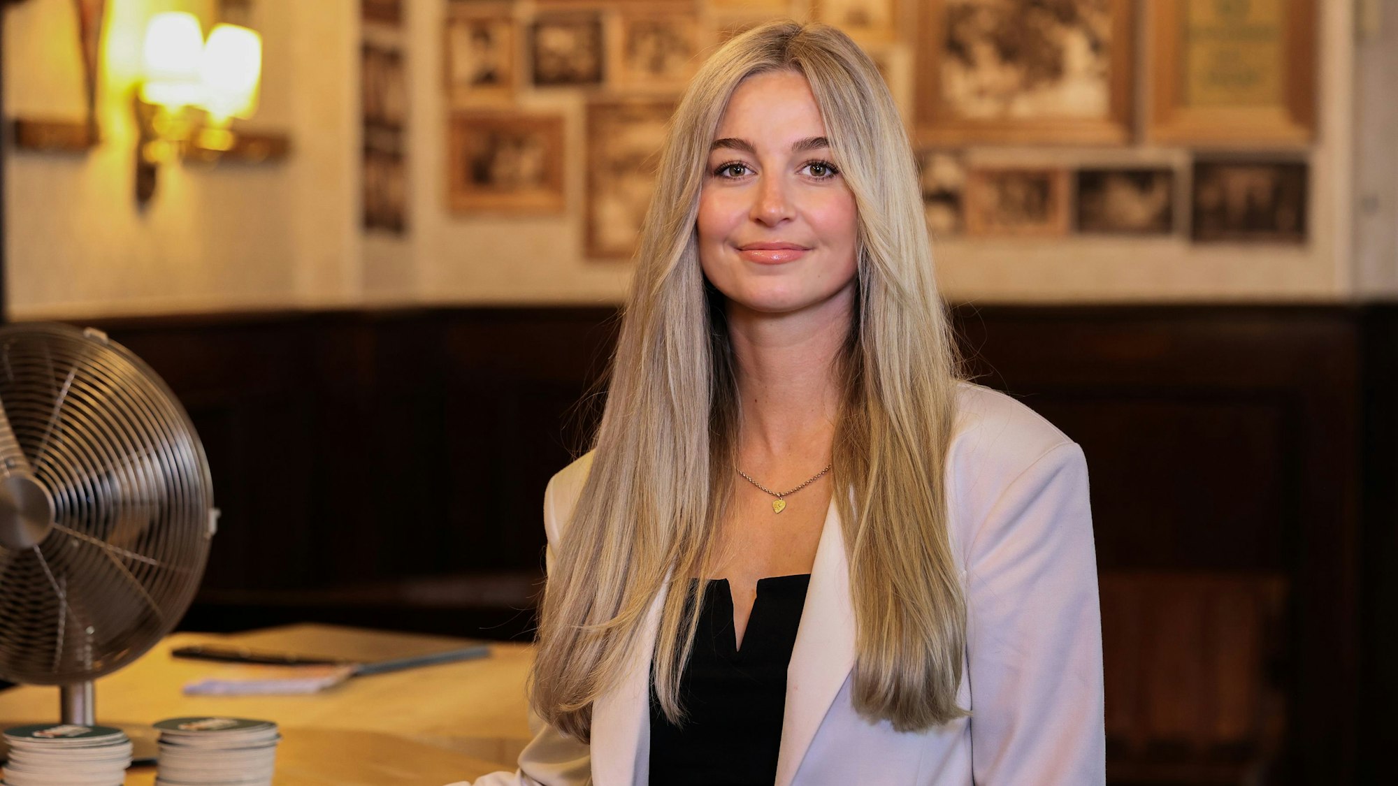 Eine Frau mit blonden langen Haaren steht vor einem Tisch mit einem Ventilator.