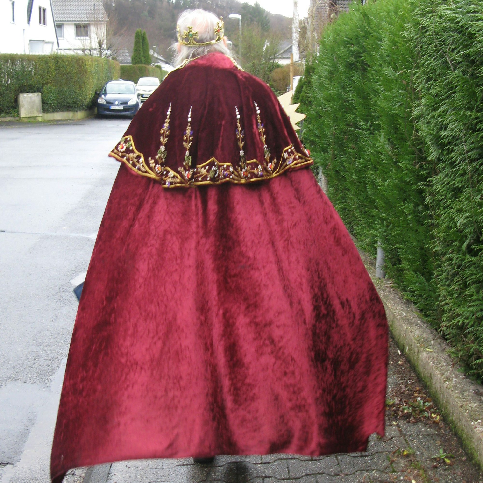 Das Bild zeigt Wolfgang Czarnecki als Heiliger König mit Krone und wehendem Umhang von hinten auf einem Bürgersteig gehend.