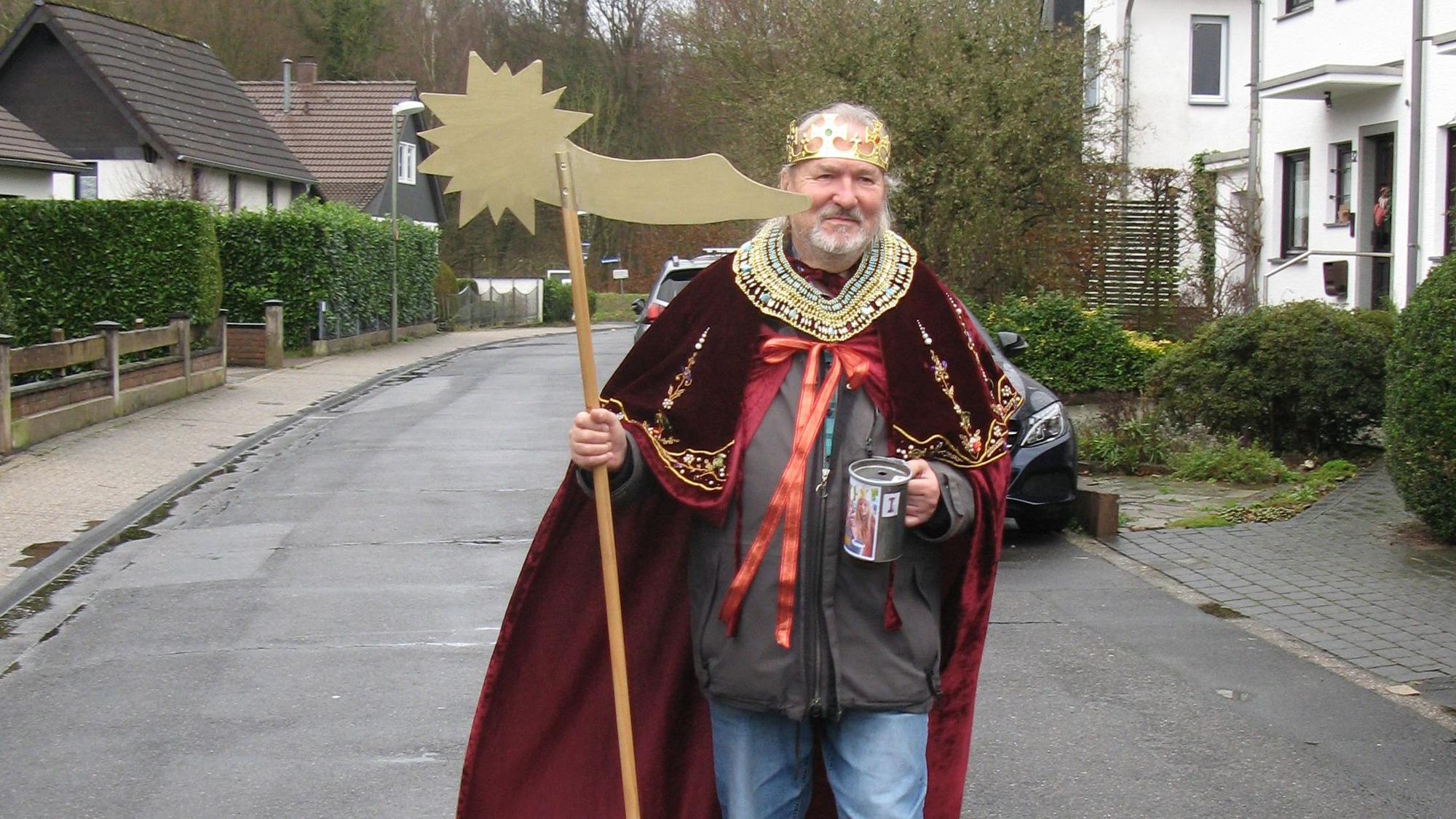 Wolfgang Czarnecki geht, verkleidet als Sternsinger, über eine Straße. In seiner rechten Hand hält er einen an einen Besenstiel befestigten Stern, in der linken seine Spendensammelbüchse.
