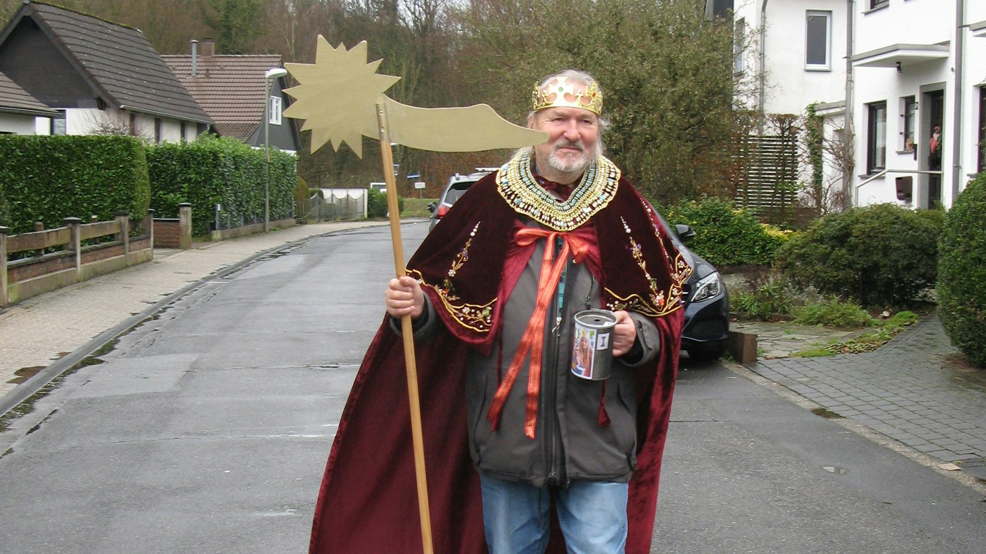 Wolfgang Czarnecki geht, verkleidet als Sternsinger, über eine Straße. In seiner rechten Hand hält er einen an einen Besenstiel befestigten Stern, in der linken seine Spendensammelbüchse.