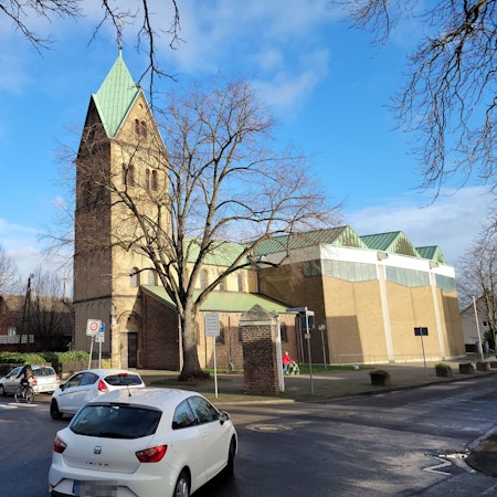 Auf einer Kreuzung  biegen zwei Fahrzeuge nach links ab, im Hintergrund ist eine Kirche zu sehen.