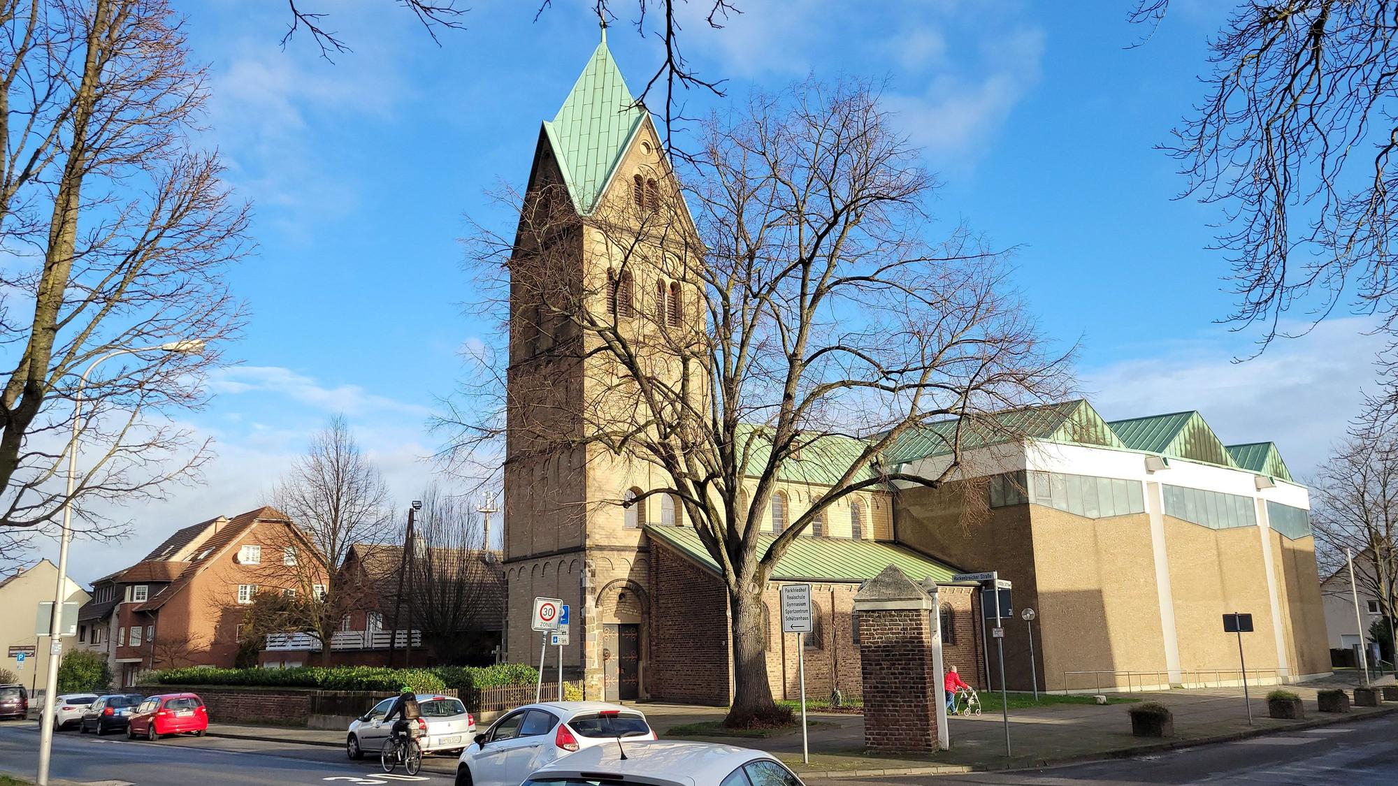 Auf einer Kreuzung biegen zwei Fahrzeuge nach links ab, im Hintergrund ist eine Kirche zu sehen.