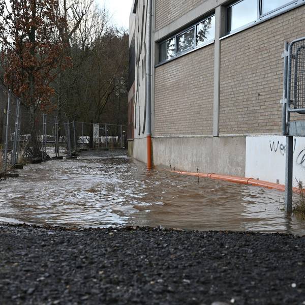 Links hinter einem Bauzaun ist die Olef in Schleiden. Der Fluss führt Hochwasser, das Wasser reicht bis ans Sturmius-Gymnasium heran.