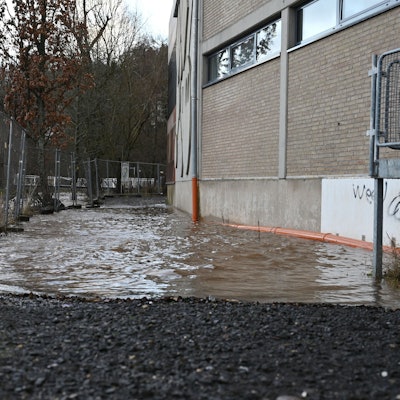 Links hinter einem Bauzaun ist die Olef in Schleiden. Der Fluss führt Hochwasser, das Wasser reicht bis ans Sturmius-Gymnasium heran.