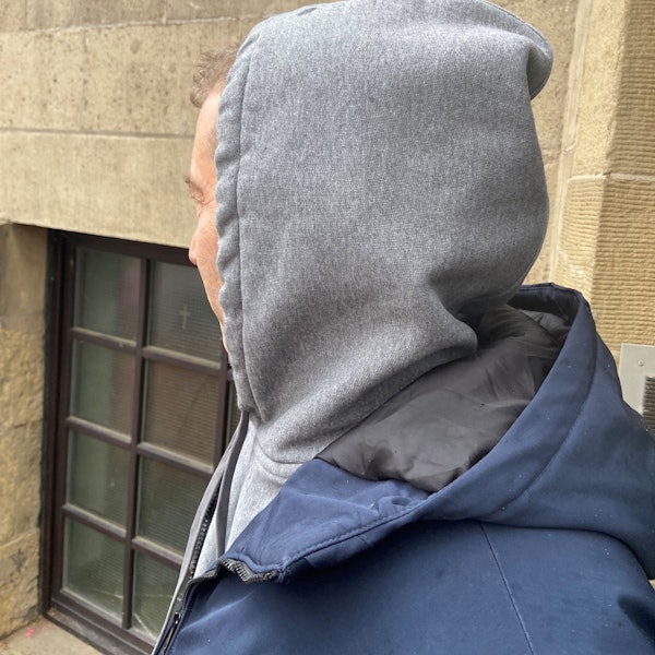 Zu sehen ist ein Mann mit Kapuze von Hinten.