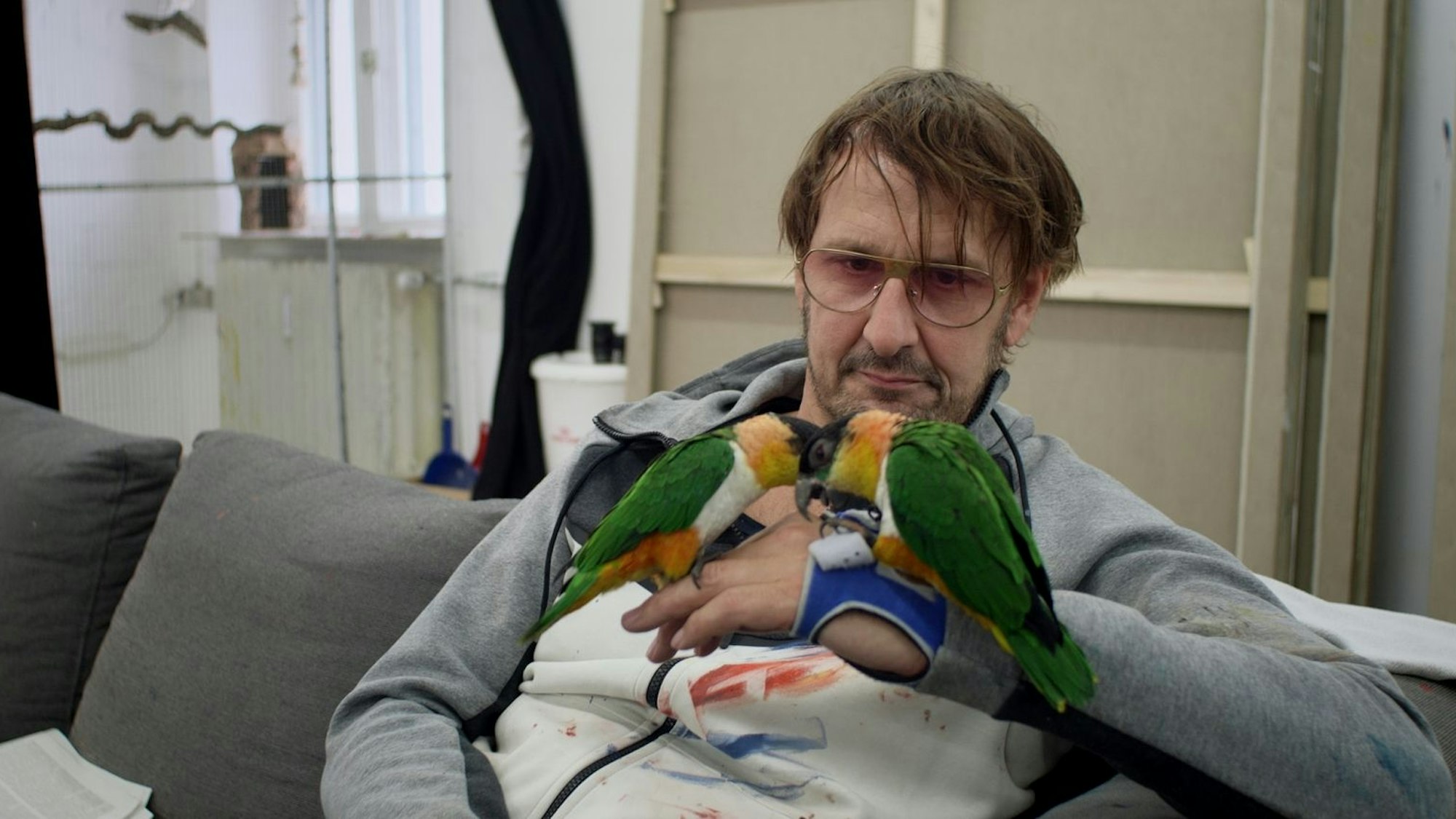 Zu sehen ist Künstler Daniel Richter, auf dessen Hand zwei Papageien sitzen.