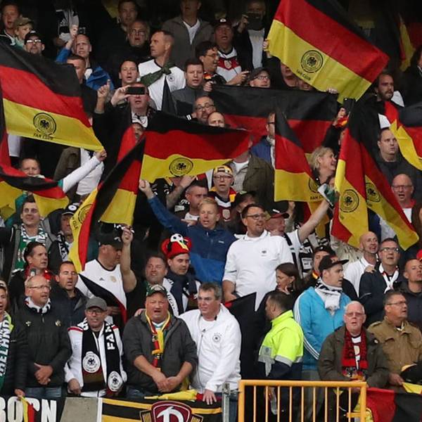 Fußball-Fans aus Deutschland stehen auf einer Tribüne und schwenken Flaggen.
