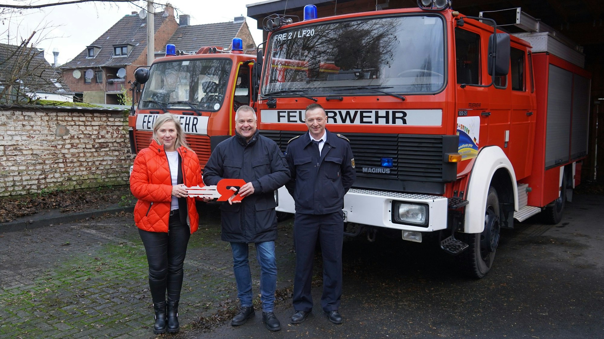 Drei Personen stehen vor zwei Feuerwehrfahrzeugen.
