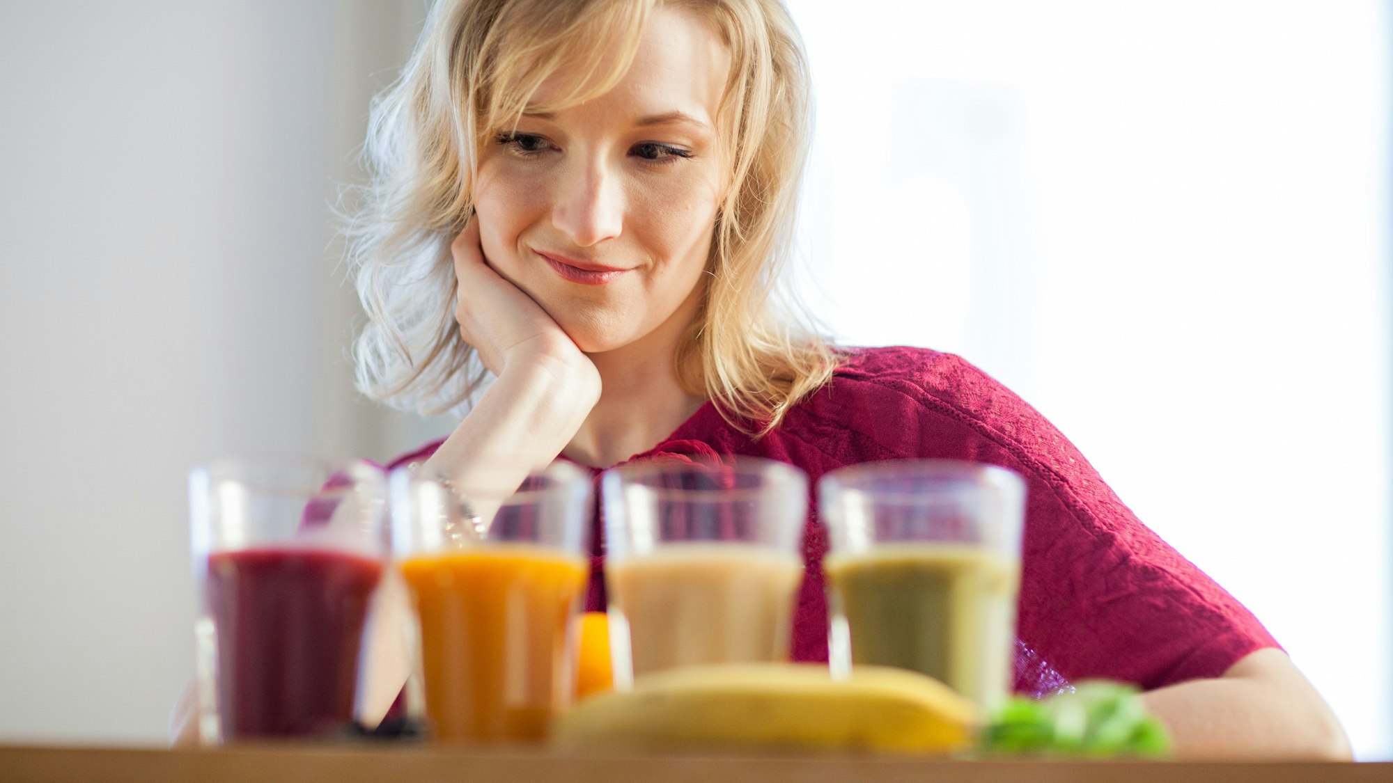 Eine blonde Frau blickt auf vier Säfte unterschiedlicher Farbe.