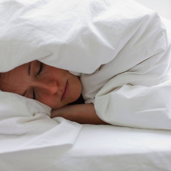 Kranke Frau liegt im Bett und zieht sich die Decke über den Kopf